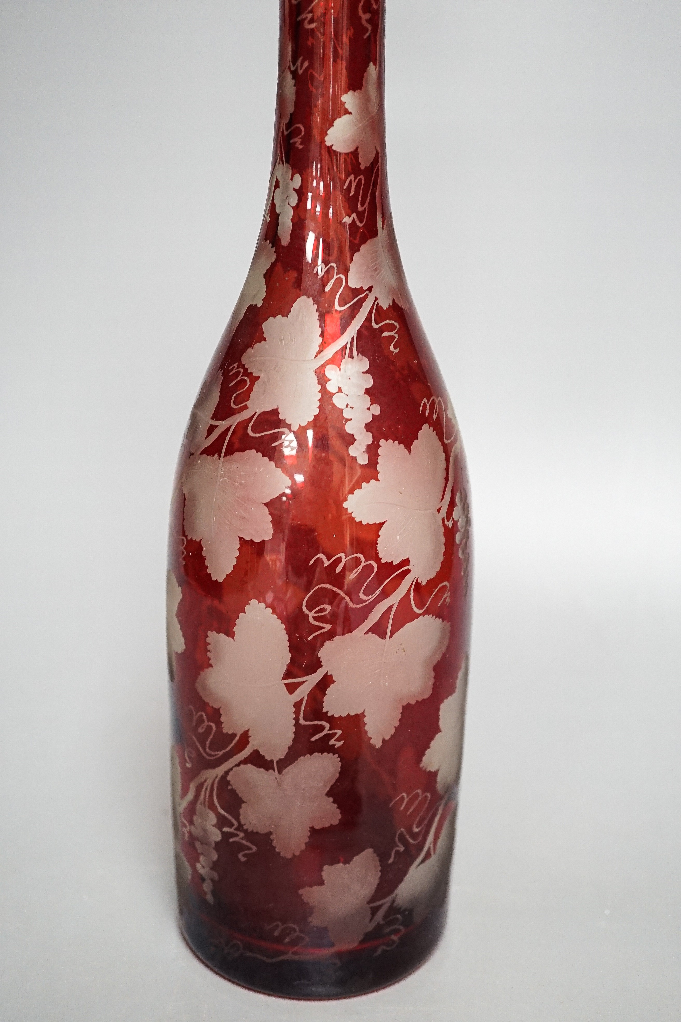 A late 19th century Bohemian wheel engraved ruby glass decanter and a pair of continental porcelain figures, decanter 37 cms high, including stopper.